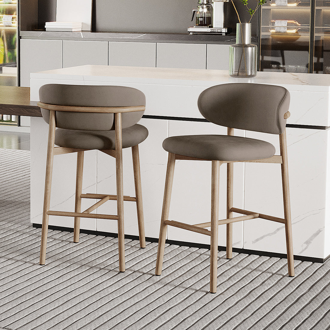 Audrey Velvet Fabric Upholstered Barstool Set of 2 with grayish-taupe curved backs, light wood legs, and a white marble counter, complementing a modern kitchen with a coffee maker and plant vase nearby.