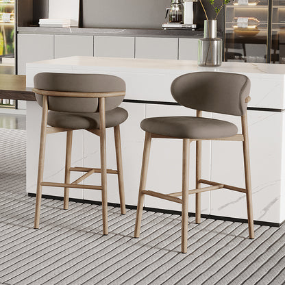 Audrey Velvet Fabric Upholstered Barstool Set of 2 with grayish-taupe curved backs, light wood legs, and a white marble counter, complementing a modern kitchen with a coffee maker and plant vase nearby.