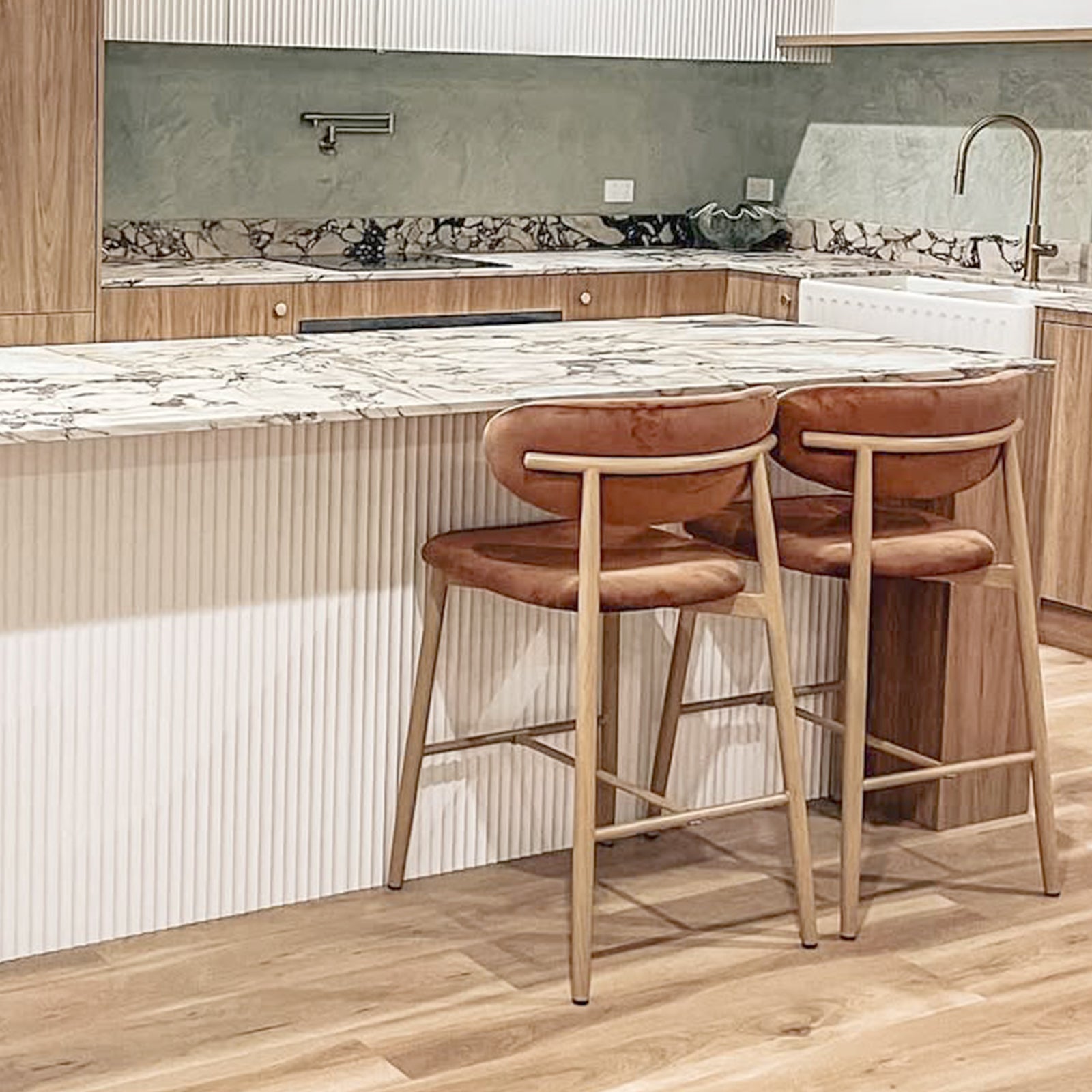 Audrey Velvet Barstool Set of 2 in Mocha Mousse features rust-colored upholstered seats, mid-century modern style, light wood frames, and contoured backs, complementing a contemporary kitchen island setting.