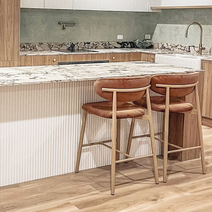 Audrey Velvet Barstool Set of 2 in Mocha Mousse features rust-colored upholstered seats, mid-century modern style, light wood frames, and contoured backs, complementing a contemporary kitchen island setting.