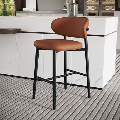 Audrey Curved PU Leather Barstool Set of 2 in Tan features a burnt-orange upholstered seat and backrest on sleek black metal legs, placed at a white marble-veined kitchen island.