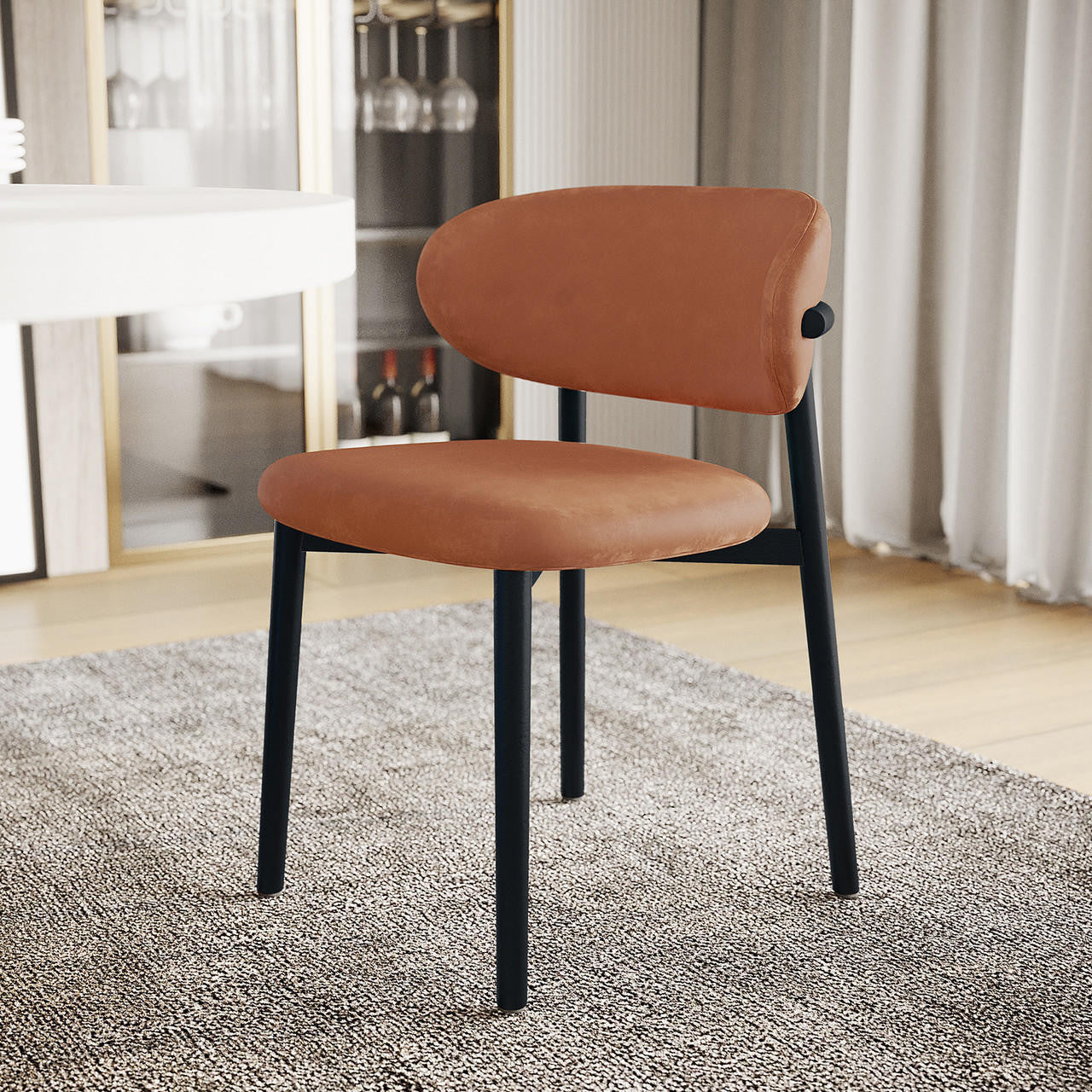 Audrey Curved Leather Dining Chair Set of 2 in Tan features rounded terracotta upholstery, slim black metal legs, on a gray rug, with a nearby white table and glass-fronted cabinet backdrop.