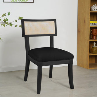 Avelino Hardwood & Rattan Dining Chair Set of 2 in Black, featuring a black wooden frame, woven cane backrest, and padded black upholstered seat, situated in a modern interior with light tiled flooring.
