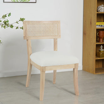 Avelino Hardwood & Rattan Dining Chair Set of 2 in Cream features a light wood frame, woven cane backrest, and padded white upholstered seat, elegantly placed on a pale tile floor.