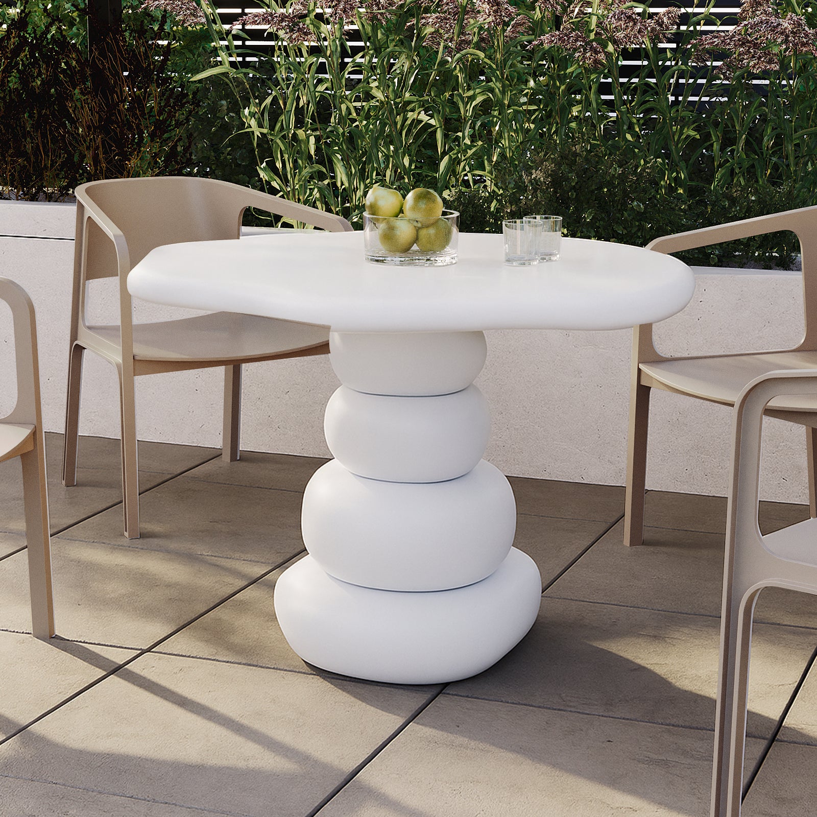 Azalea Round Indoor/Outdoor Concrete Dining Table White with a sculptural base, surrounded by modern chairs on a patio. A glass bowl with green apples and glasses adorns the tabletop.