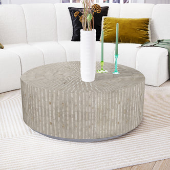 Baltoy 100cm Mother of Pearl Coffee Table in Striped Bone, featuring a textured, stone-like surface, is the centerpiece amidst a modern living room setup with a ceramic vase and taper candles.