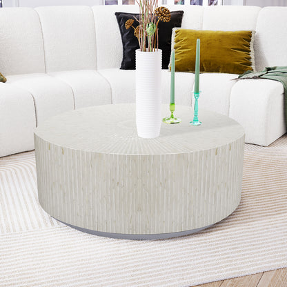 Baltoy 100cm Mother of Pearl Inlay Coffee Table in Sand, featuring a round design with intricate inlay, sits elegantly on a light-striped rug, surrounded by decor in a modern living area.