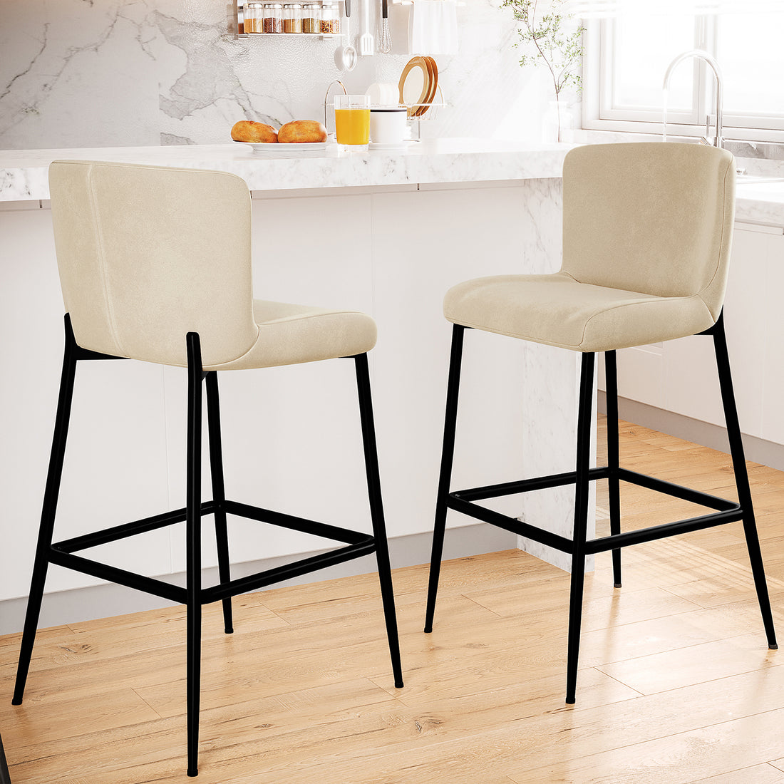 Bernie High Back Velvet Bar Stool Set of 2 in Oatmeal, featuring lightly upholstered beige seats, matte-black metal legs with footrests, positioned by a marble-topped island in a bright kitchen setting.