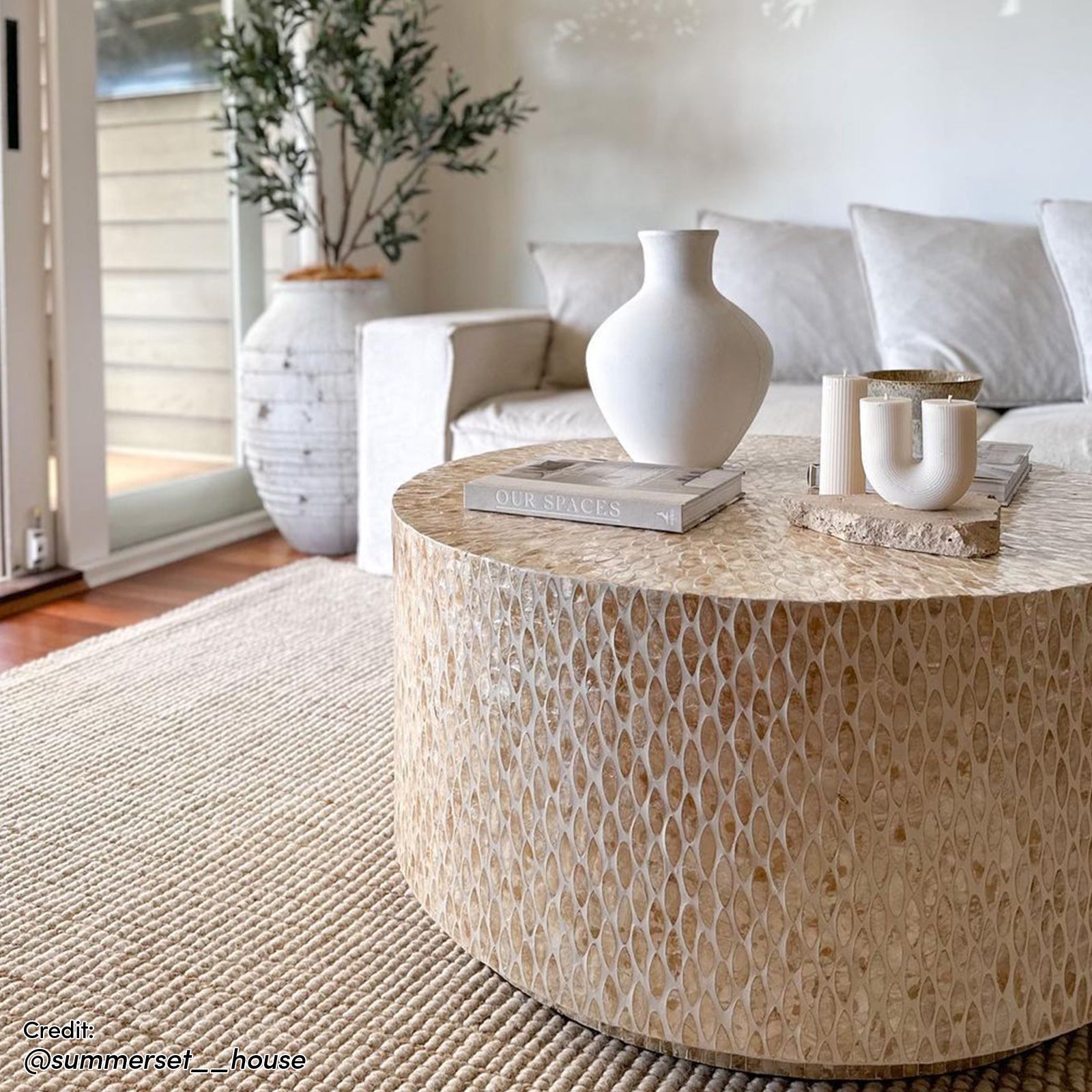 The Bisera 91cm Mother of Pearl Inlay Coffee Table features a hand-crafted, intricate mother-of-pearl mosaic on its surface, set in a stylish living room environment with complementary decor.