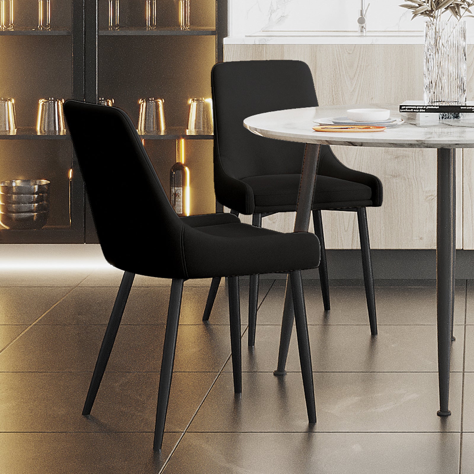 Blythe Velvet Dining Chair Set of 2 in Black with slim metal legs around a marble-top table, featuring a clean, contemporary design with a vase and tableware on display.