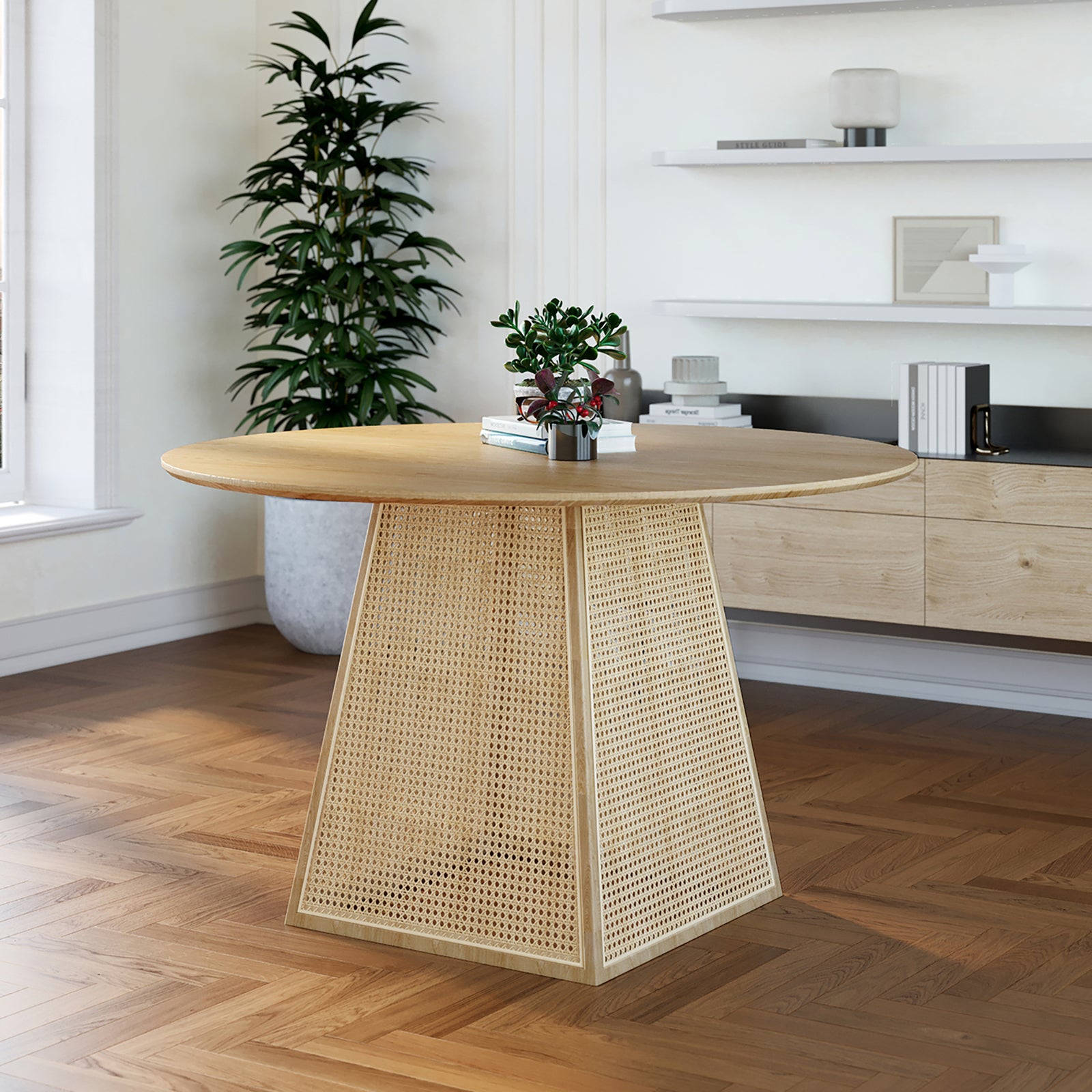 Casey 120cm Round Rattan Dining Table features a round wooden tabletop with a woven cane-panel pedestal base, styled with books and a succulent, in a minimal, bright interior setting.