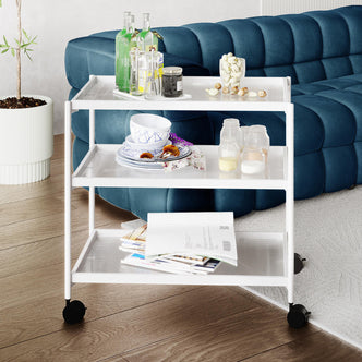 Chelsea 3-Tier Fluted Glass Drink Cart Bar Trolley in White featuring three metal-framed tiers with fluted glass, showcasing bottles, glassware, spices, and magazines. It includes four wheels for mobility.