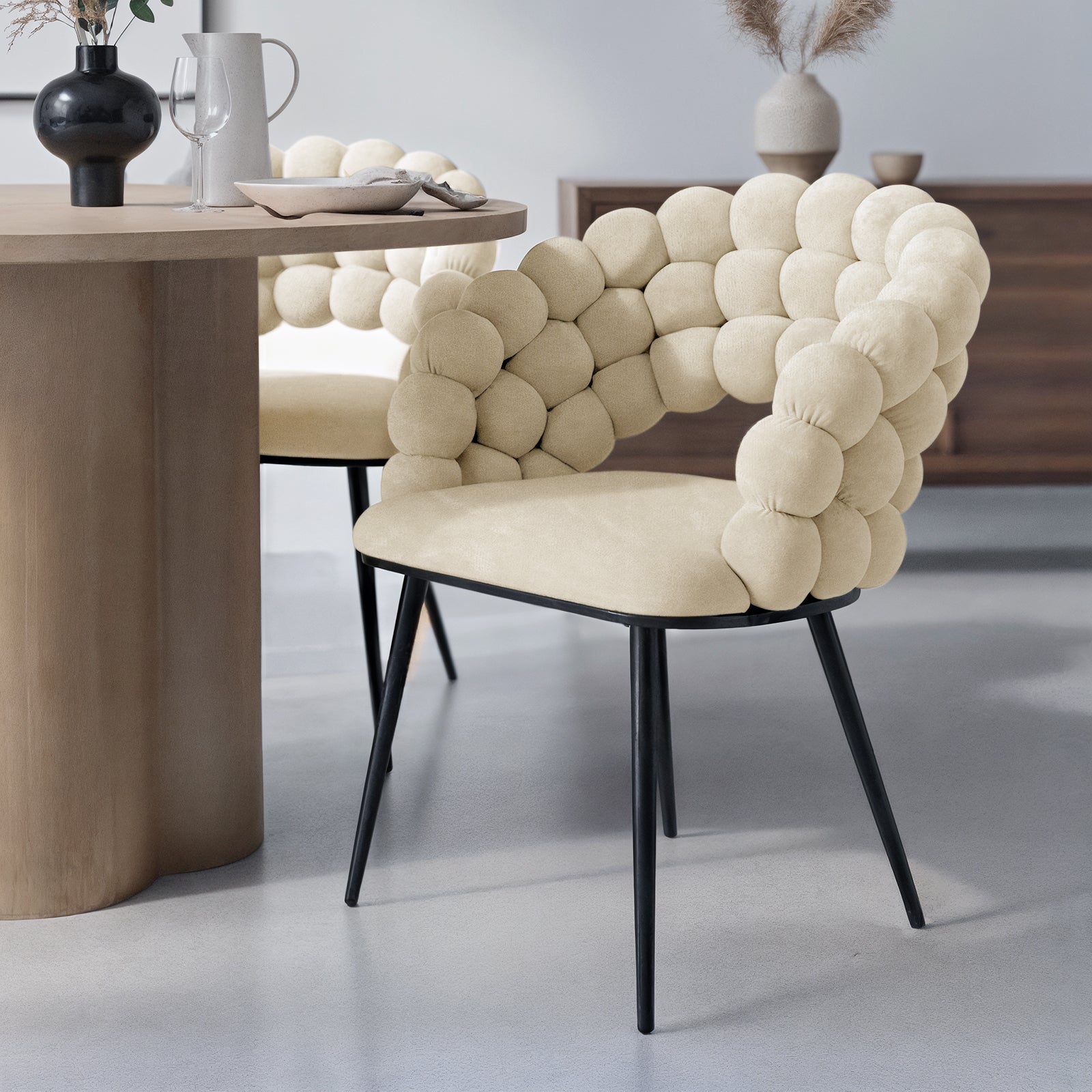 Claudine Velvet Curved Dining Chair Set of 2 in Oatmeal, featuring bubble-style upholstery on black metal legs, paired with a round dining table, creating a modern and elegant dining nook.