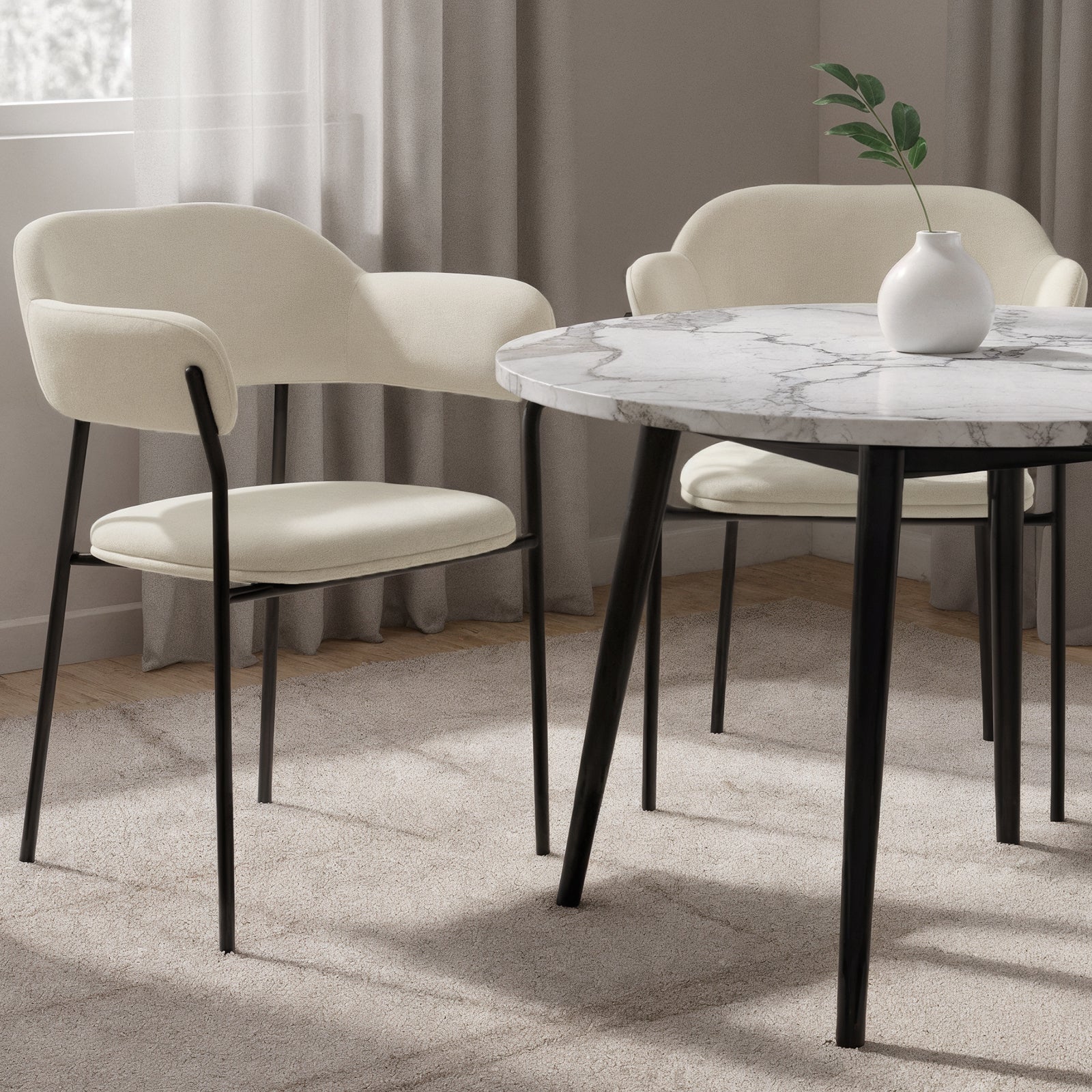Clavin Fabric Dining Chair Set of 2 in Light Beige, featuring cream upholstery on slender black metal legs, with gently curved backs and seat pads, surrounding a modern marble-effect table.