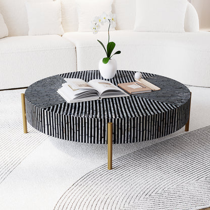 Cradily Mother of Pearl Inlay Coffee Table in Ivory & Black with mosaic pattern tabletop, brass legs, open book, notebook with pen, decorative sphere, orchid vase, plush sofa, and detailed rug backdrop.