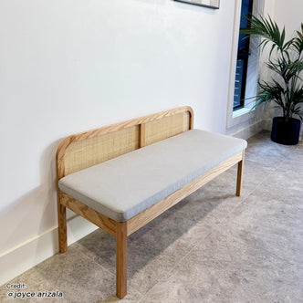 Dana 120cm Solid Oak Hardwood Bench with Backrest features a sturdy oak frame and natural rattan backrest, positioned stylishly on a tile floor with a houseplant nearby.