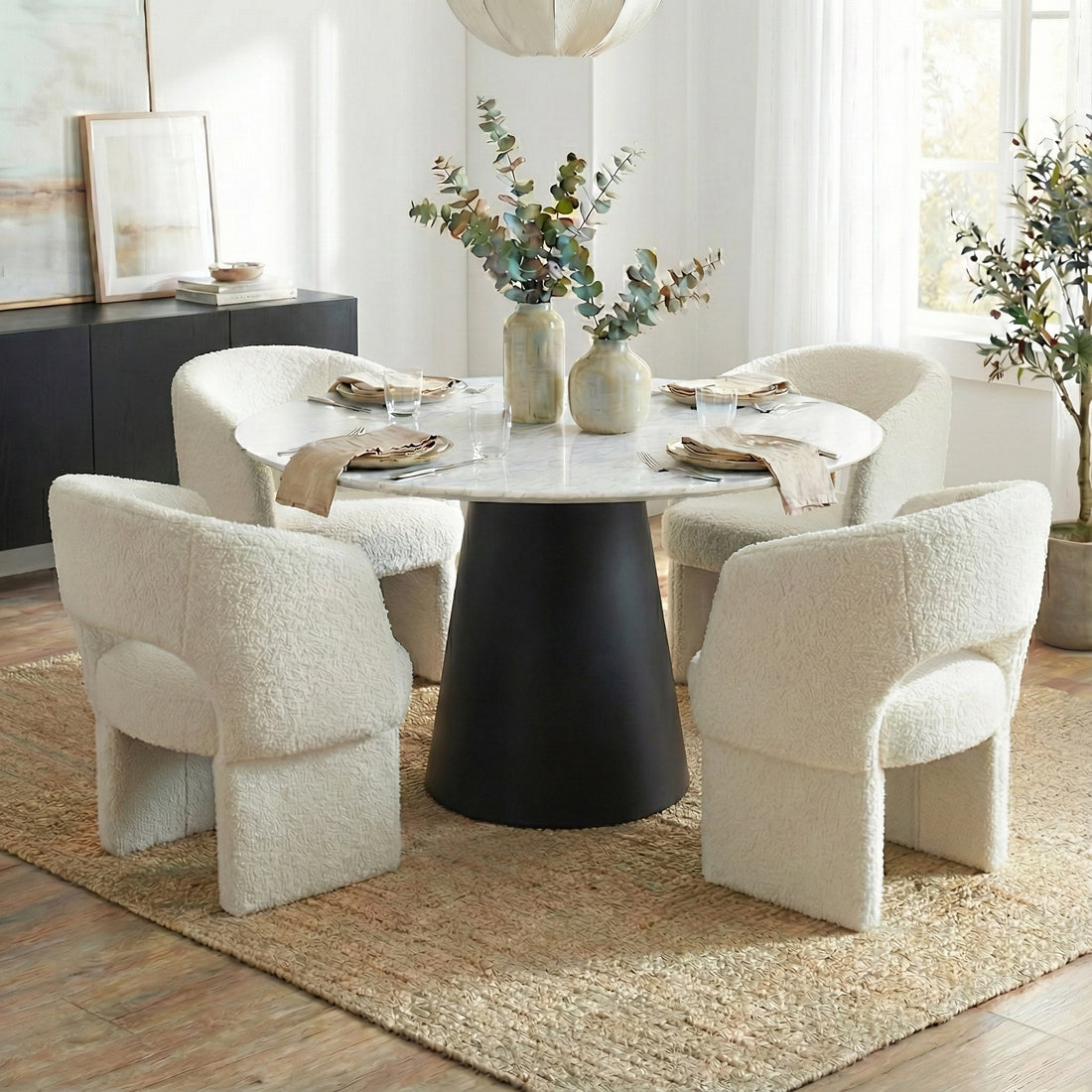 Dina 120cm Round Marble Dining Table in Real Carrara Black features a white marble top with blue-grey veining on a black pedestal, paired with off-white boucle armchairs and set elegantly for dining.