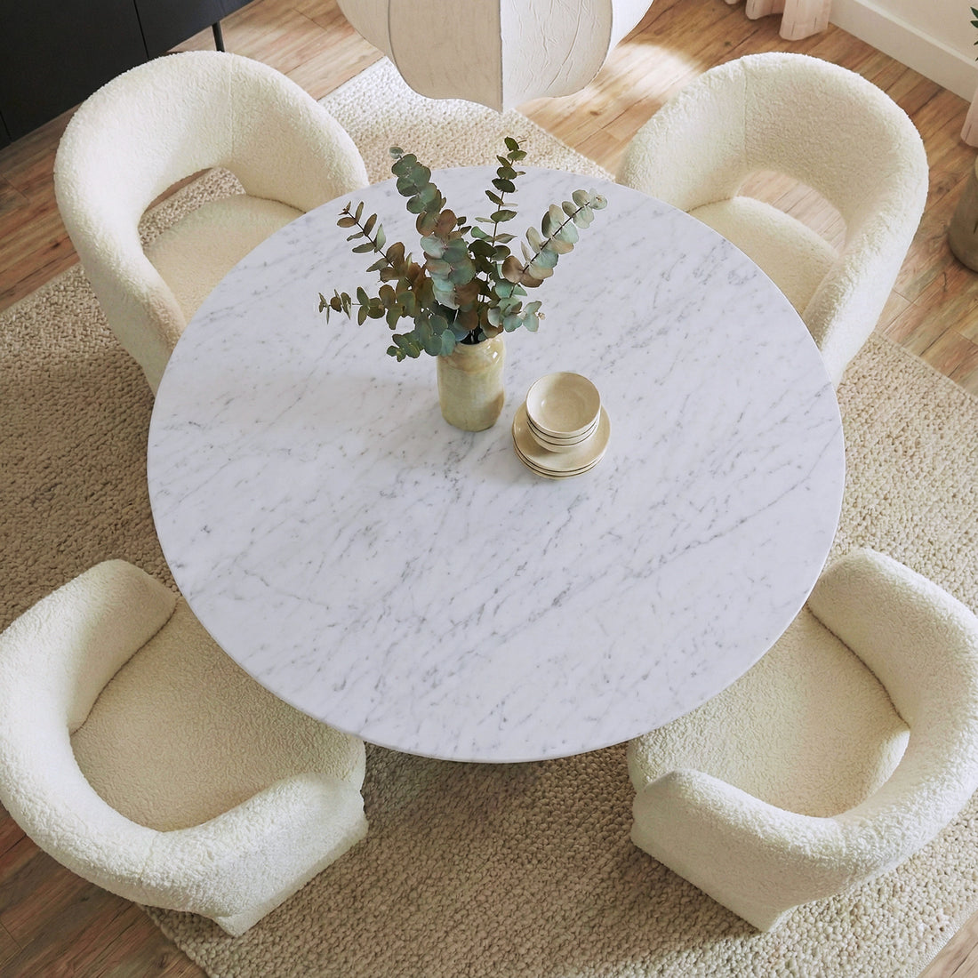 Dina 120cm Round Marble Dining Table in Real Carrara Black, featuring a white marble top with unique veining and an ash wood base, surrounded by ivory boucle armchairs on a woven rug.
