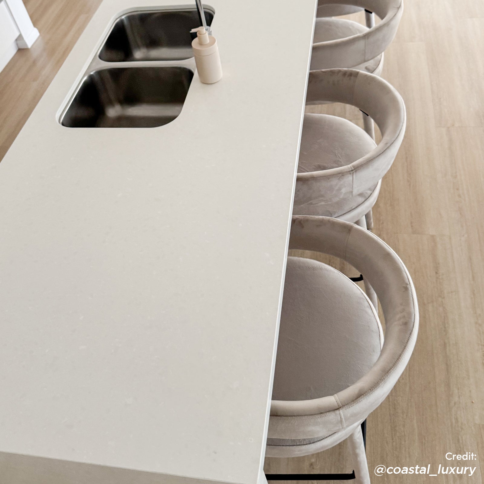 Eisha Velvet Bar Stool Set of 2 in Beige, featuring plush velvet upholstery, curved backrests, and sturdy powder-coated metal legs, elegantly tucked under a modern kitchen island with a white quartz countertop.