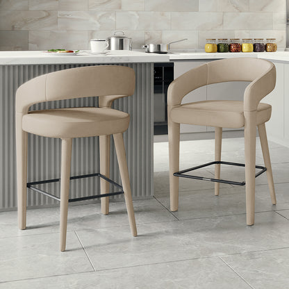 Eisha Velvet Bar Stool Warm Grey Set of 2, featuring a modern design with curved backs and armrests, positioned next to a counter, showcasing their upholstered velvet finish and built-in footrests.