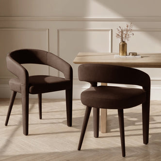 Eisha Velvet Dining Chair Set of 2 in Deep Mocha Brown, featuring rounded seats and curved backs, paired with a light-wood table, brass-tone vase, and marble tray, in a contemporary setting.