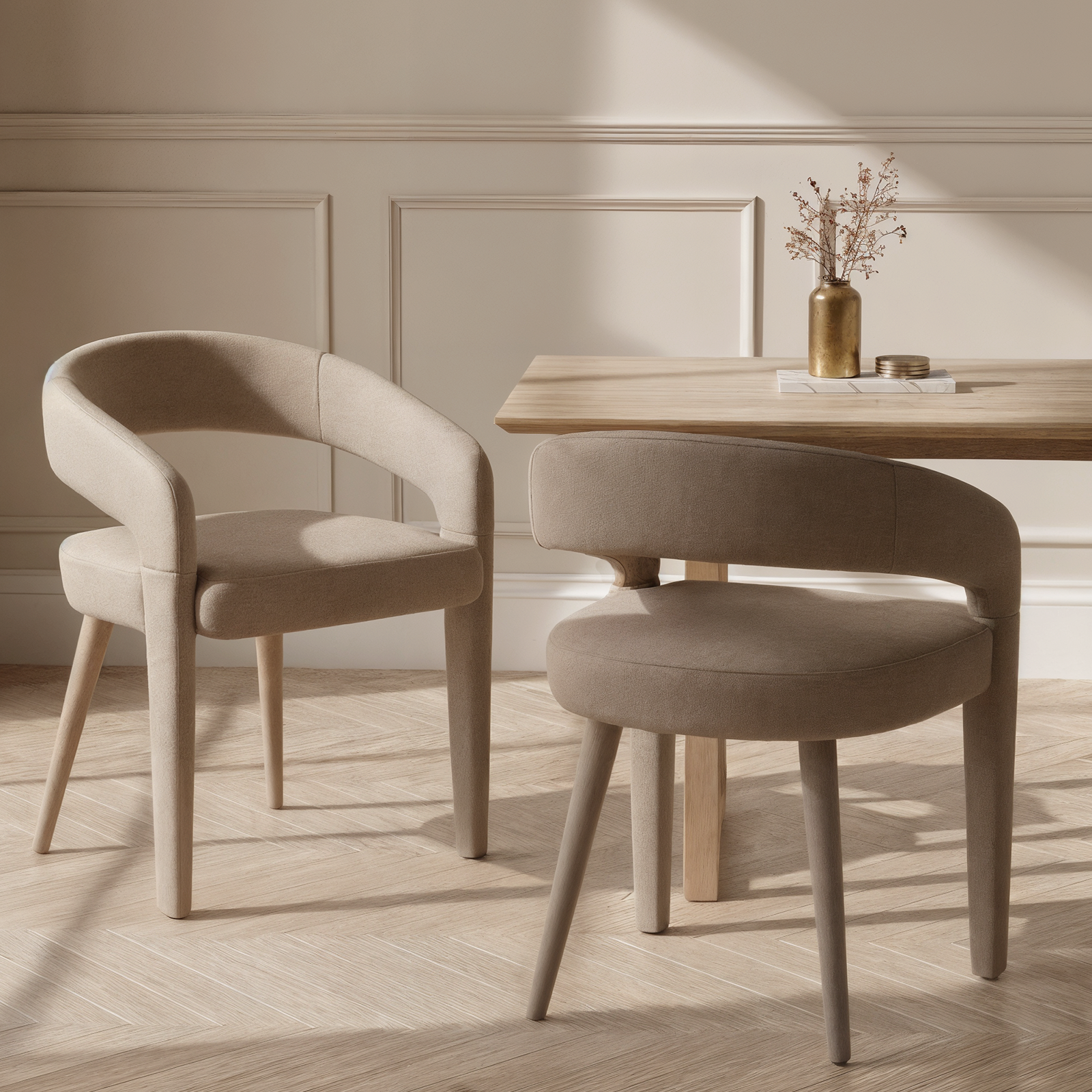 Eisha Velvet Dining Chair Set of 2 in warm grey, featuring plush velvet upholstery and supportive curved backrests, complements a minimalist nook with wooden table and decorative elements.