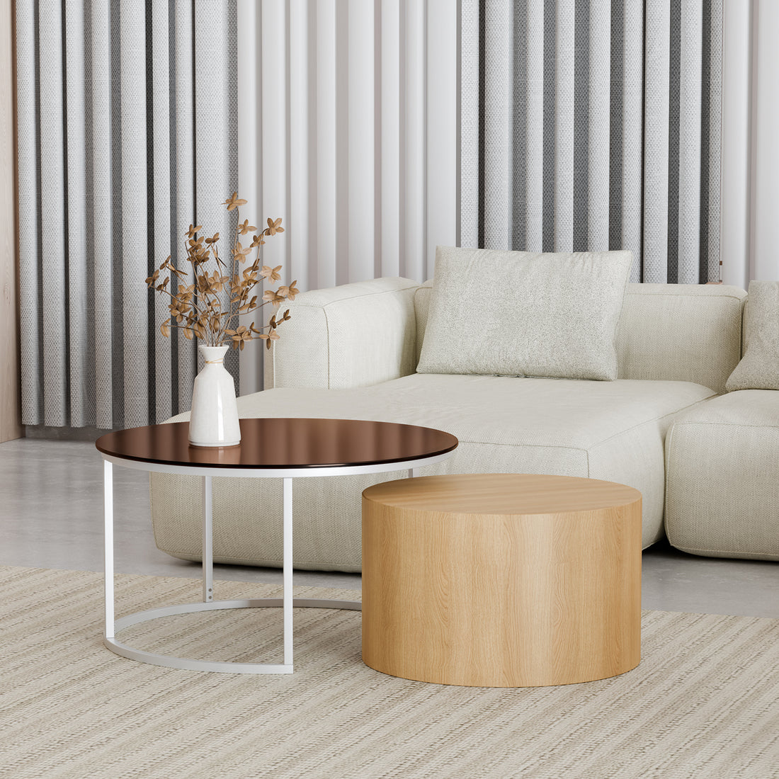 Ellisha Round Nesting Coffee Table in Natural, featuring a light wood cylindrical drum and dark-stained top on a sleek white metal frame, adorned with a white vase and dried foliage.