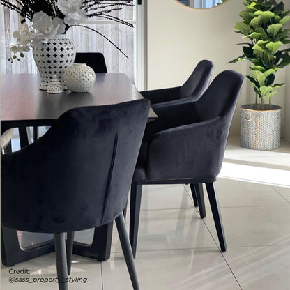 Elly Velvet Curved Dining Chair with Arms (Set of 2) – Black, featuring a curved high-back design with integrated armrests and tapered metal legs, exuding contemporary elegance and comfort.