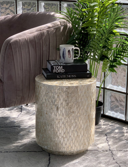 Ely 40cm Mother of Pearl Inlay Side Table in Beige with mosaic surface, topped with two books and a feather-painted mug, beside a dusty rose velvet sofa and green plant.