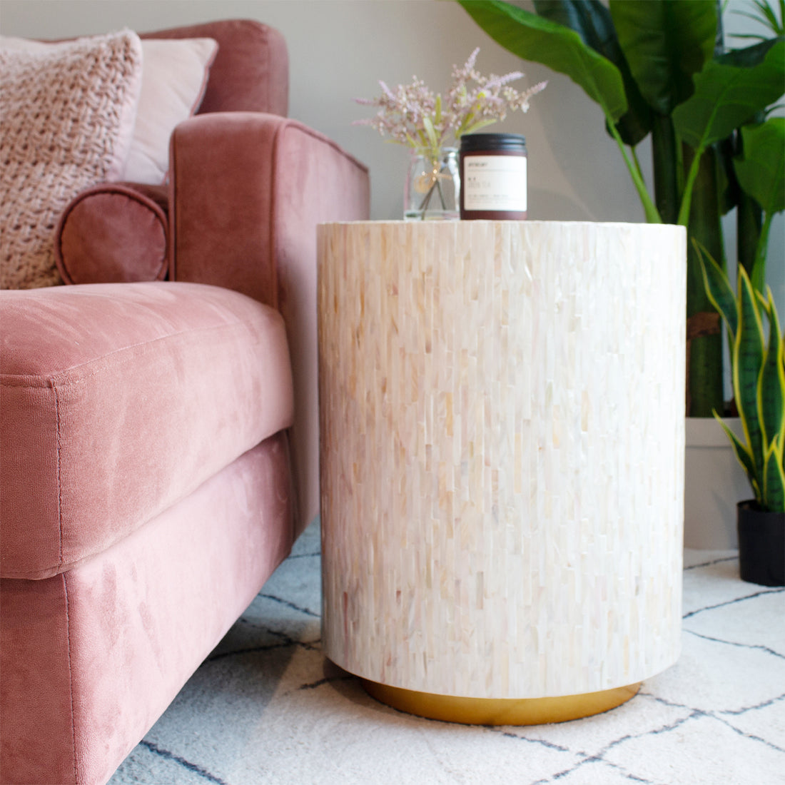 Ely 40cm Mother of Pearl Inlay Side Table in Cream beside a dusty-rose sofa, featuring a handcrafted mosaic surface and brass-toned base, topped with lavender sprigs and an amber candle jar.