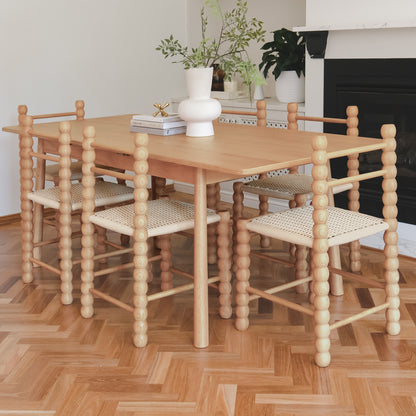 Em Solid Oak Dining Chair Set of 2 - Natural showcased around a wooden table, featuring distinctive beaded posts and woven seats, enhancing the light-filled dining area with rustic charm and modern appeal.