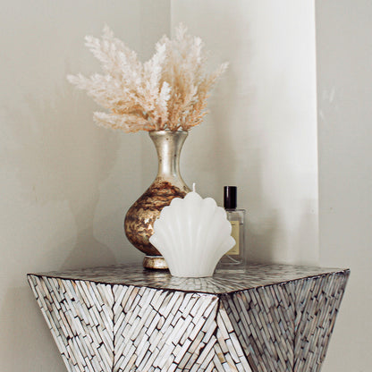 Enki 35cm Mother of Pearl Inlay Side Table in Beige & Black with mosaic detailing, showcasing a metallic vase with pampas grass, scallop shell candle, and glass perfume bottle against a neutral backdrop.