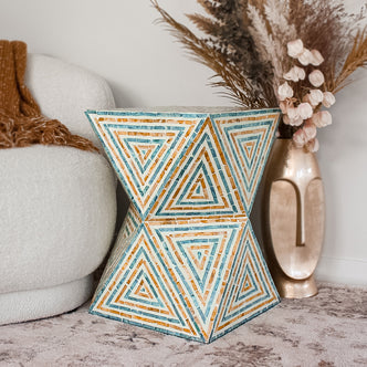 Enki 35cm Mother of Pearl Inlay Side Table in Orange & Blue, featuring a mosaic of concentric triangles, stands in a cozy living room vignette with a boucle chair and gold vase.