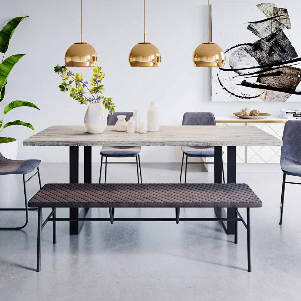 Ernest 200cm 6 Seater Industrial Dining Table in Natural, featuring a rectangular light-gray wood tabletop with black metal U-shaped legs, complemented by matching bench and upholstered chairs, under brass pendant lights.