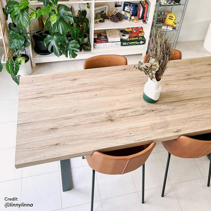 Ernest 200cm 6 Seater Industrial Dining Table in Natural, showcasing a weathered-oak finish and slim-legged design, with U-shaped legs, complemented by tan leatherette chairs in a sleek, modern setting.