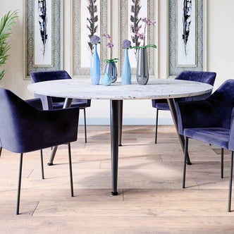 Eugene 120cm 4 Seater Round Dining Table in Marble features a sleek white-marble top with black metal legs, surrounded by elegant blue velvet chairs, creating a stylish, modern dining nook.