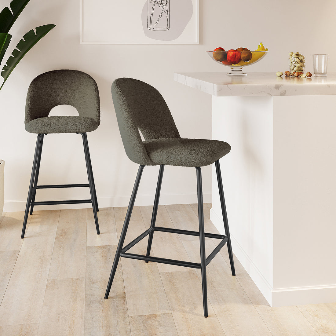Evie High Back Boucle Bar Stool Set of 2 in Green features olive-green upholstered seats with cut-out backs on black metal frames, positioned at a modern kitchen island with marble-style countertops and light wooden flooring.