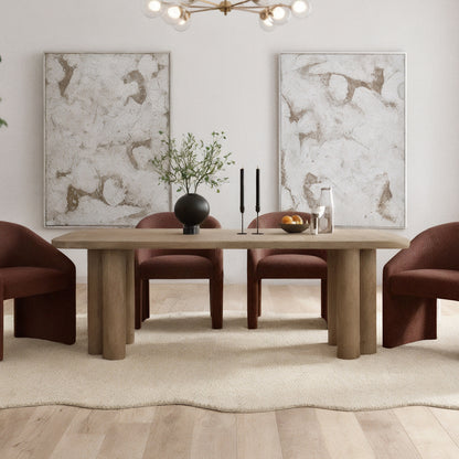 Faunus 200cm 8 Seater Dining Table in Natural with chunky cylindrical legs, centered on a pale rug, surrounded by rust-upholstered chairs, adorned with a black vase, candles, and a fruit bowl.