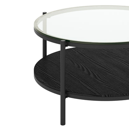 Frances 80cm Round Tempered Glass Coffee Table in Black features a clear glass top with a sleek black metal frame, dark-stained wood lower shelf, supported by slender cylindrical legs.