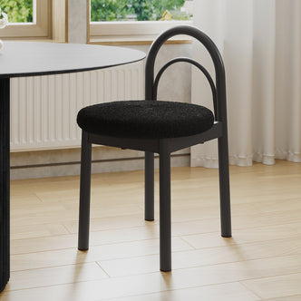 Gilles Boucle Arched Dining Chair Black Set of 2, featuring a double-arched backrest and upholstered seat, positioned next to a dining table, highlighting its elegant design and sturdy metal construction.