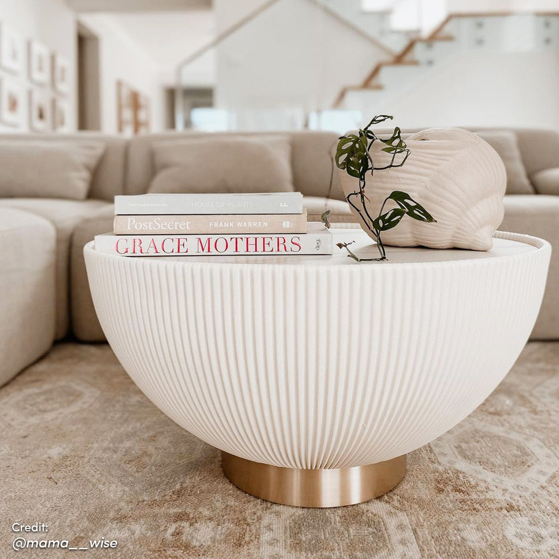 Glalie 70cm Sintered Stone Coffee Table Cream White with fluted surface, brass-tone base, topped with books and ceramic vessel holding Monstera adansonii, styled in a minimalist living room vignette.
