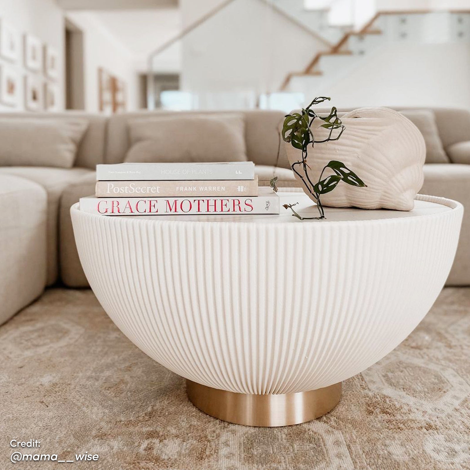 Glalie 70cm Sintered Stone Coffee Table Cream White with fluted surface, brass-tone base, topped with books and ceramic vessel holding Monstera adansonii, styled in a minimalist living room vignette.