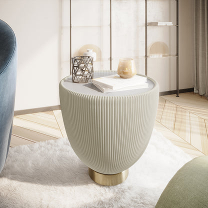 Glalie 47cm Sintered Stone Coffee Table in Cream White features a ribbed urn-like base on a brass pedestal, topped with decor items, set on a plush faux-fur rug in a modern space.