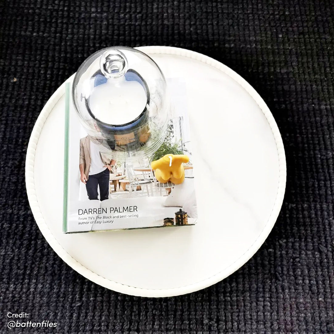Glalie 47cm Sintered Stone Coffee Table in Cream White, styled with a white tray, design book, glass cloche, and yellow decorative object on a dark rug, viewed from above.