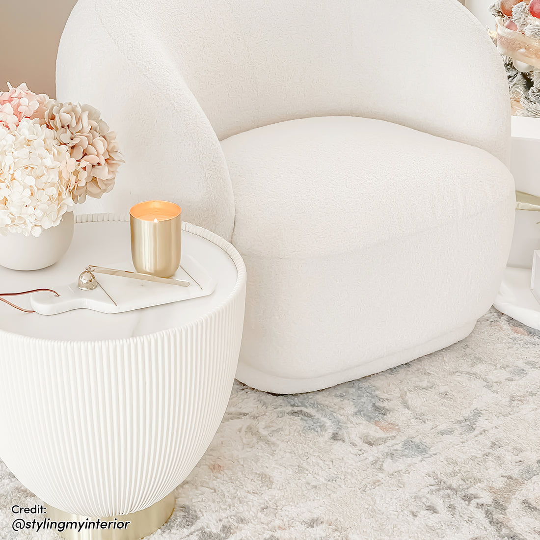 Glalie 47cm Sintered Stone Coffee Table in Cream White, featured with a rounded design and brass-tone base, complements the cozy nook with a boucle armchair and decorative accents.