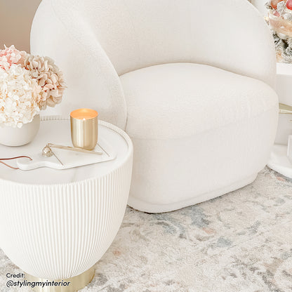 Glalie 47cm Sintered Stone Coffee Table in Cream White, featured with a rounded design and brass-tone base, complements the cozy nook with a boucle armchair and decorative accents.
