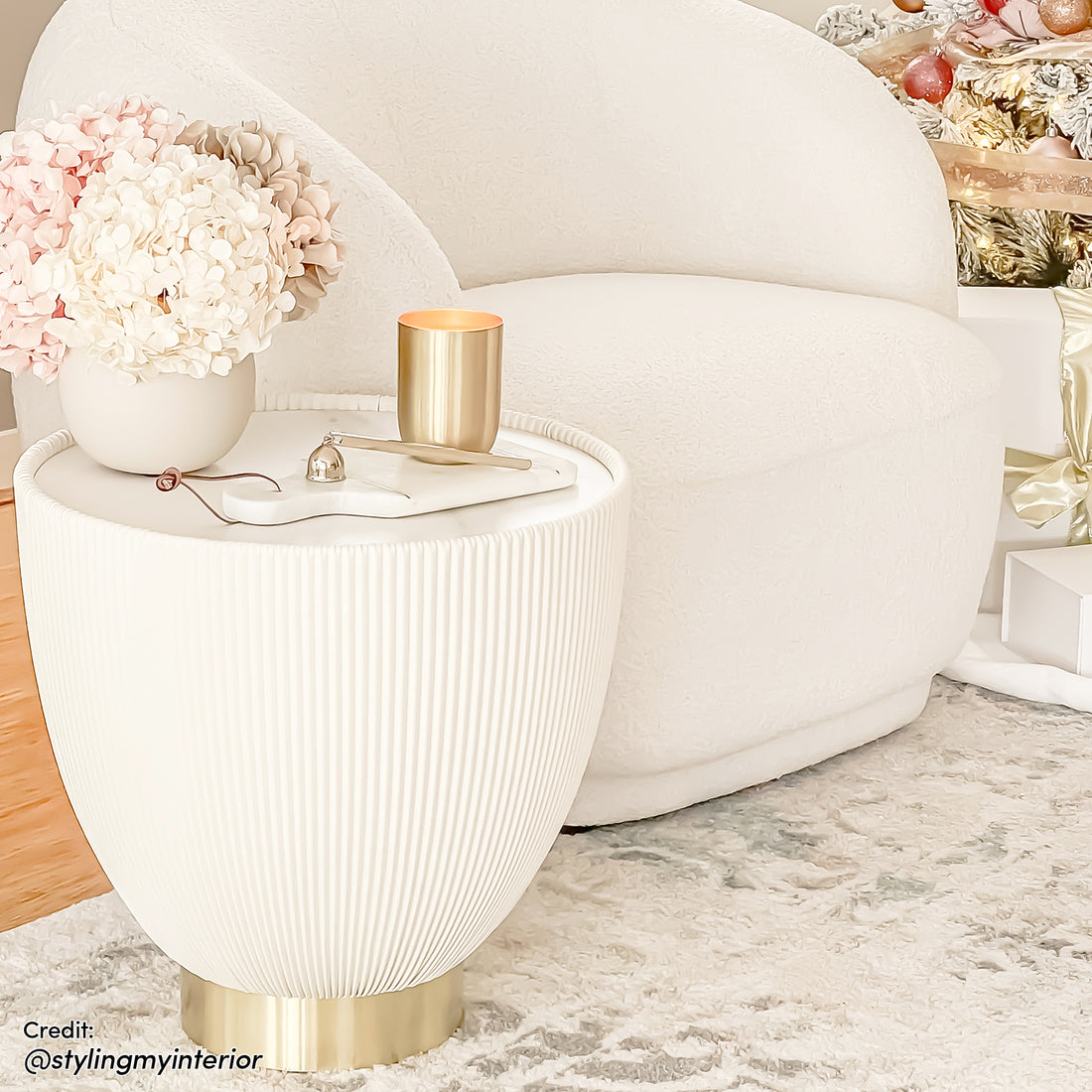 Glalie 47cm Sintered Stone Coffee Table in Cream White, featuring a round, fluted design with a polished brass base, topped with a vase of hydrangeas, a candle, and a marble tray.