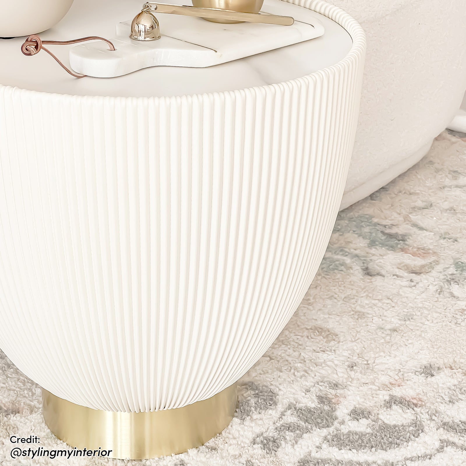 Glalie 47cm Sintered Stone Coffee Table in Cream White with a softly rounded, fluted design, sits on a brass base, topped with a marble board and gold-tone accessories.