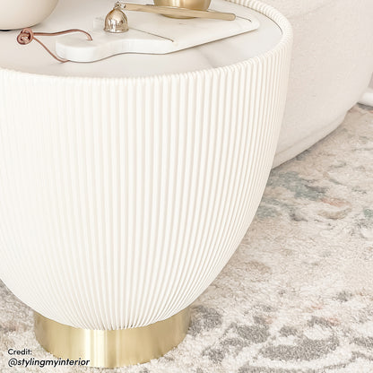 Glalie 47cm Sintered Stone Coffee Table in Cream White with a softly rounded, fluted design, sits on a brass base, topped with a marble board and gold-tone accessories.