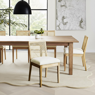 Gretel Hardwood & Rattan Dining Chair Set of 2 in Natural, featuring woven cane backs and cushioned seats, is elegantly arranged around a solid-wood table in a minimalist dining area.